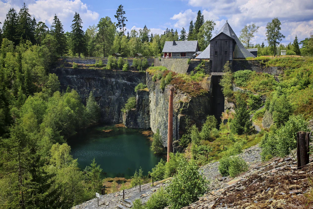 Ein malerischer Steinbruchsee, umgeben von hohen Felsen und Bäumen,: das Technische Denkmal im Schieferpark Lehesten am Rennsteig