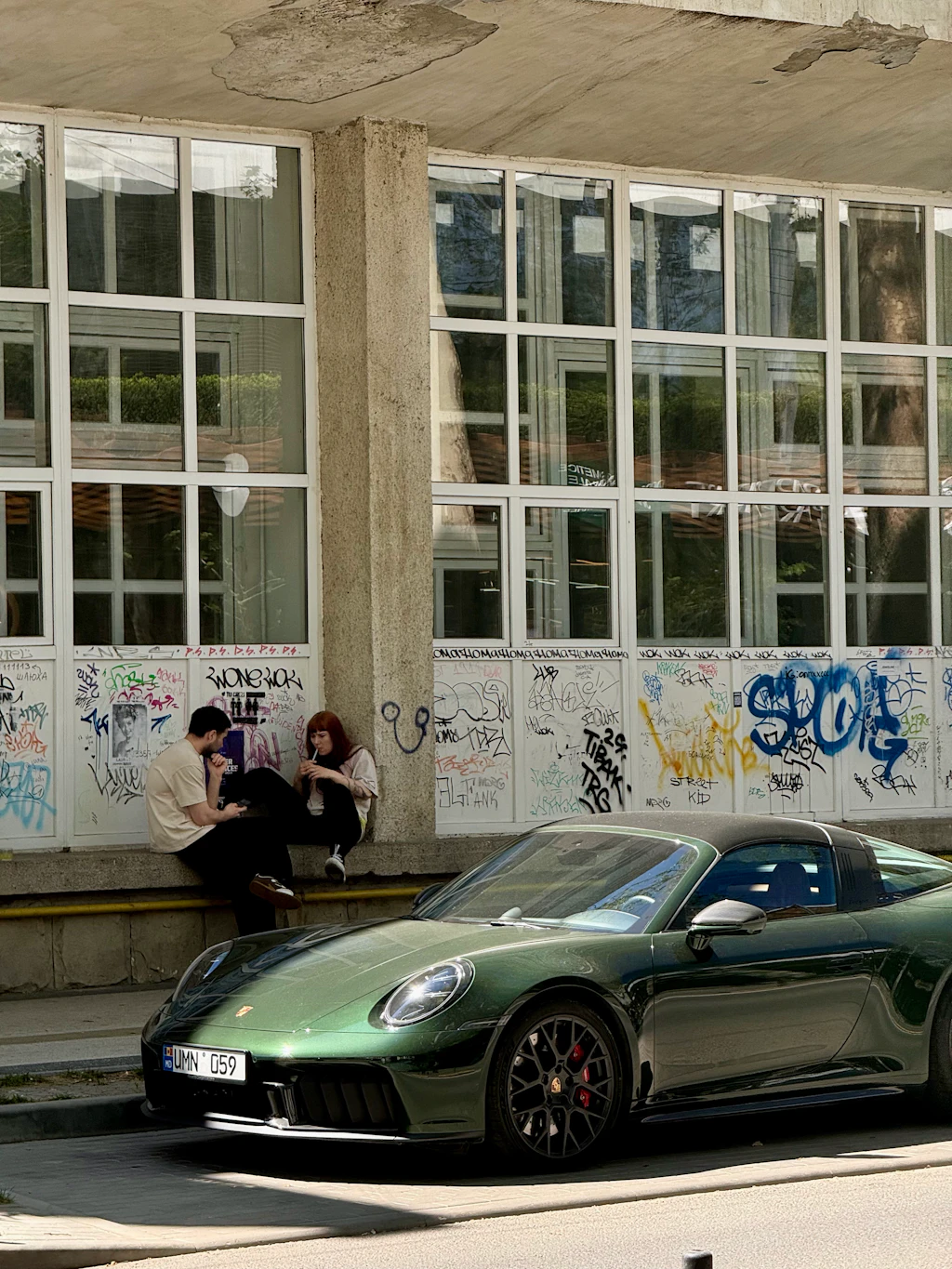 Facettenreiches Stadtleben: ein dunkelgrüner Porsche vor graffitibedeckter Sowjetfassade in Downtown Chișinău.