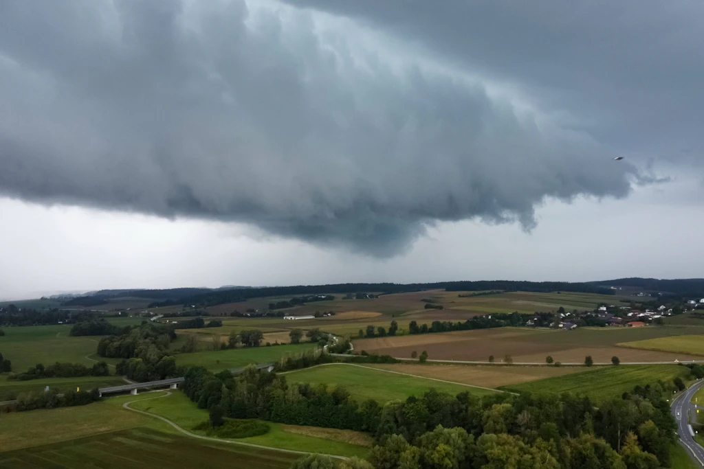 Aufziehende Wolkenfront über Feldern und Wald: Am Sonntag zieht ein Frontensystem langsam von Westen nach Südosten, im Westen sind über 20 Liter Regen pro Quadratmeter in wenigen Stunden möglich. (Symbolbild)