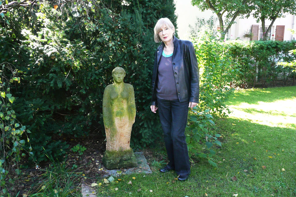 Die Bildhauerin Carin Kreuzberg (1935–2026)  mit einer ihrer Sandstein-Skulpturen in einer Pankower Grünanlage