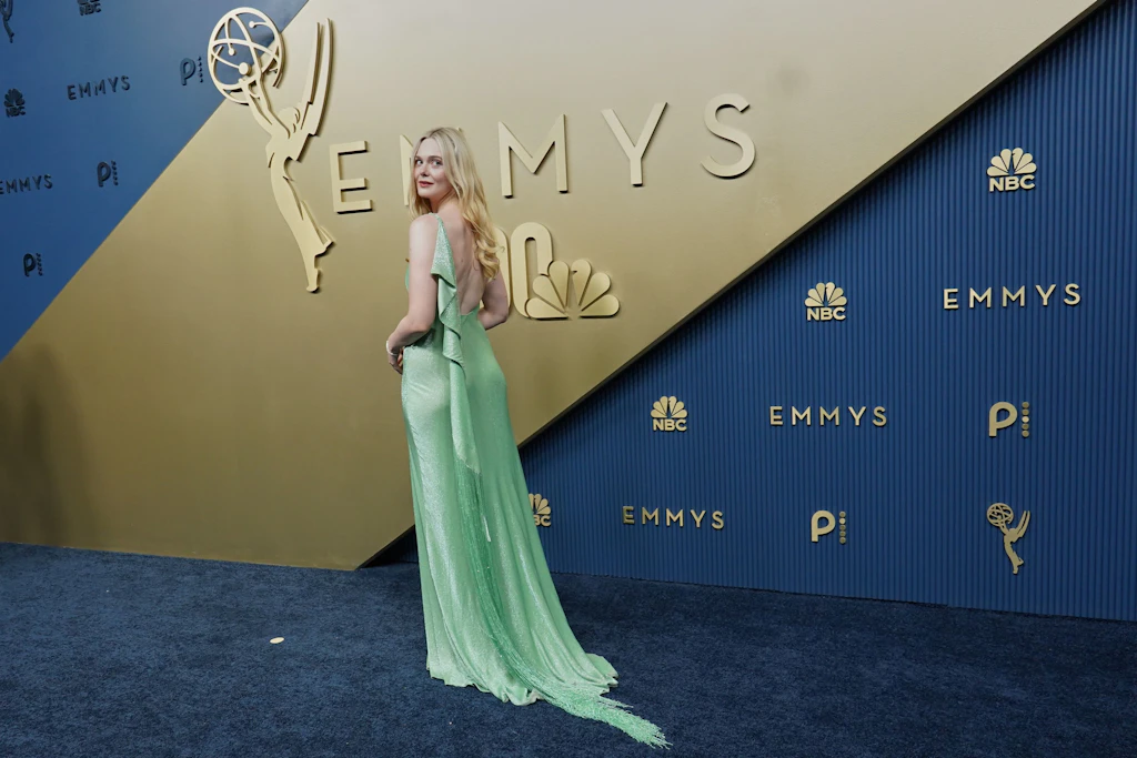 Elle Fanning zeigt die Rückseite ihres mintgrünen Kleids – die Fransenschleppe zieht sich über den Teppich.