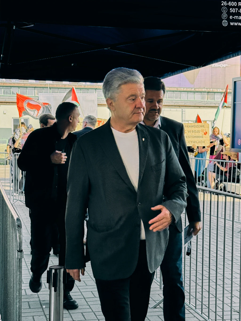 Auch ehemalige Präsidenten sind auf der MSPO unterwegs: Selenskyjs Amtsvorgänger Petro Poroschenko. Im Hintergrund protestieren Demonstranten gegen die Präsenz israelischer Aussteller.