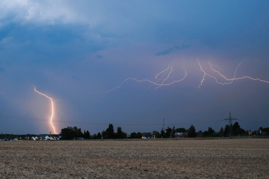 Blitze über einem abgeernteten Feld in der Abenddämmerung: Am Dienstagabend ziehen im Nordwesten teils kräftige Gewitter auf, dabei sind Sturmböen der Stärke 9 möglich. (Symbolbild)