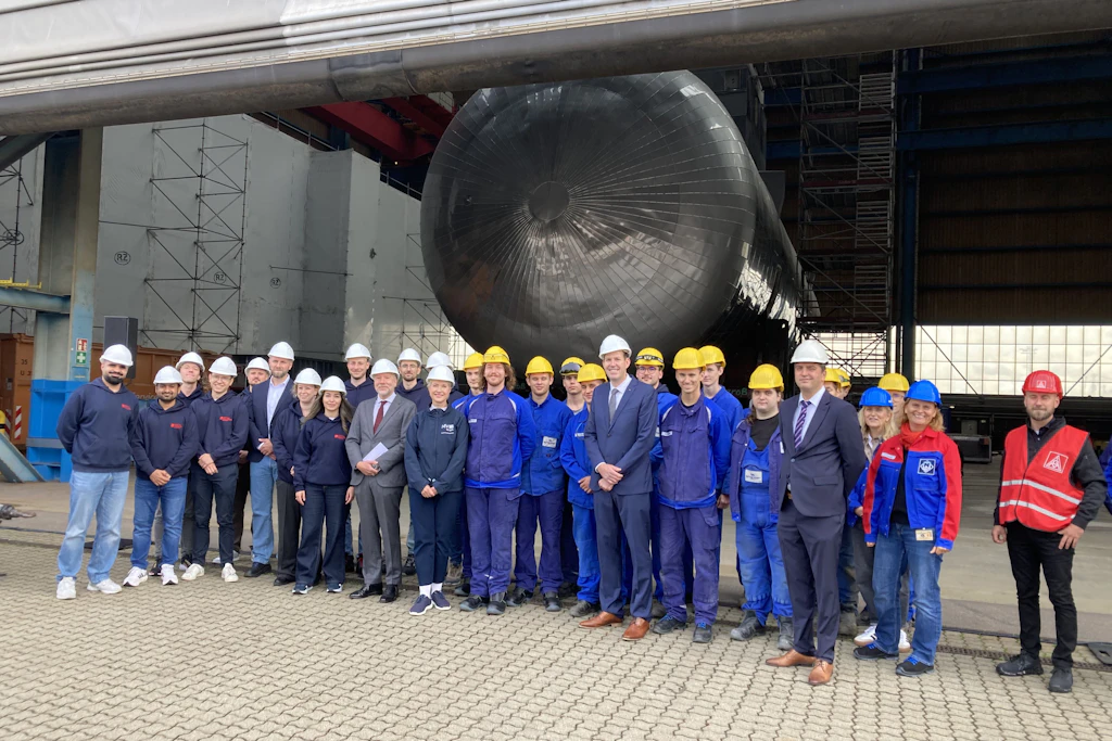 Manuela Schwesig (m.) mit den Bossen von 50Hertz und NSORe sowie Azubis der Neptunwerft und Mitgliedern einer Delegation aus Vlissingen vor einer Halle auf dem Gelände der Neptunwerft in Rostock.