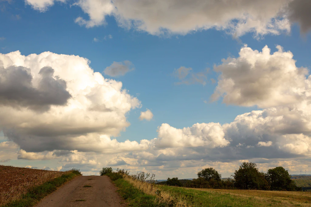 Feldweg unter Quellwolken: Im Süden bringt der Samstag Sonne und bis zu 26 Grad, im Norden stürmische Böen bis 80 km/h. (Symbolbild)