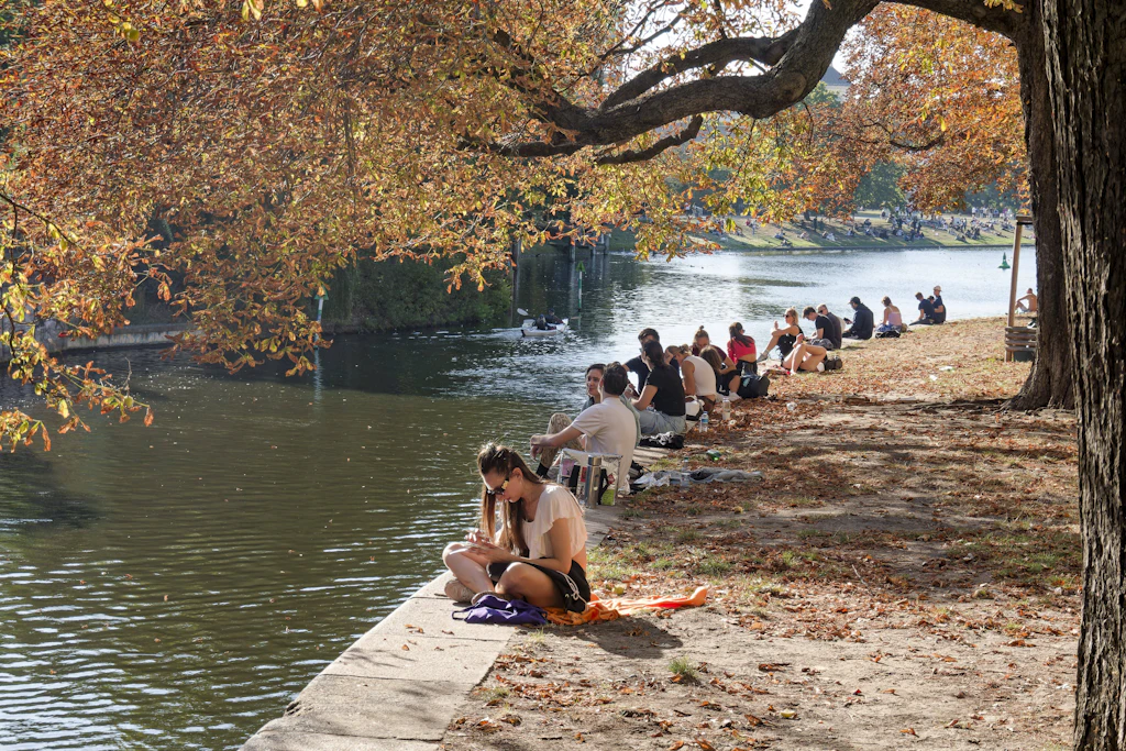 Sommer unter Herbstlaub: Menschen genießen die Sonne am Ufer. Das europäische Wettermodell berechnet für Ende September noch einmal bis zu 31 Grad. (Symbolbild)
