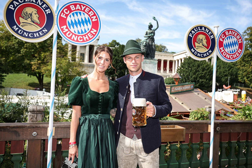 <strong>Top:</strong> FC-Bayern-Kapitän <strong>Joshua Kimmich</strong> führt nicht nur auf dem Platz – auch auf der Wiesn macht er eine gute Figur. Zur vereinseigenen Tracht kombiniert er einen grünen Filzhut, der farblich perfekt mit dem dunkelgrünen Samtdirndl von Heimatglück harmoniert, das seine Frau Lina trägt. Ein aufeinander abgestimmter Partnerlook, der wirkt, als wäre er mühelos entstanden. Fazit: Nicht nur Fußball kann er – Tracht darf er auch.