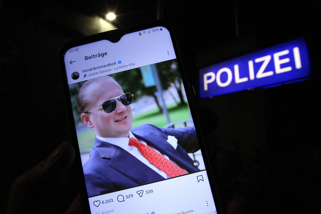 Ein Mann hält vor einem Polizeikommissariat ein Smartphone in der Hand, auf dem der Instagram-Account von Windkraftbetrüger Hendrik Holt geöffnet wurde.