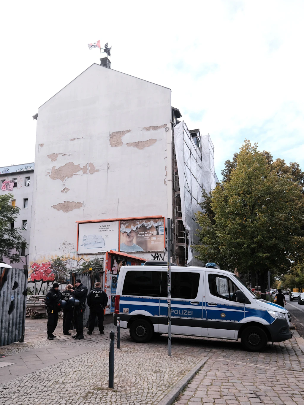 Am Donnerstagmittag ist es noch ruhig vor dem Haus: Die Flagge der Besetzer weht am Schornstein, Einsatzkräfte der Polizei sichern den Gehweg vor dem Gerüst.