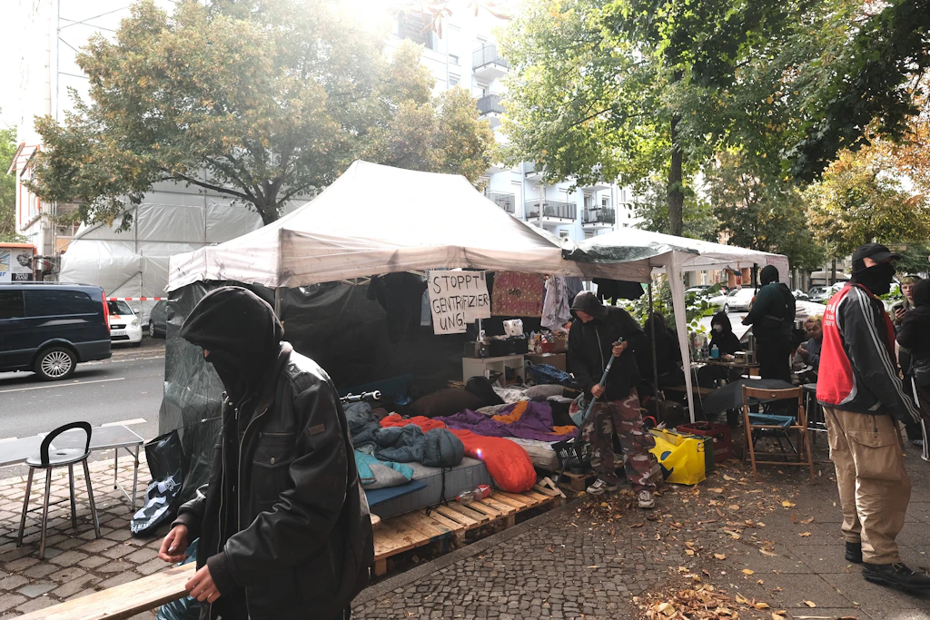 Im Vordergrund die Dauermahnwache in Form von Pavillons der ehemaligen Besetzer, im Hintergrund die eingerüstete Immobilie kurz vor der Durchsuchung.