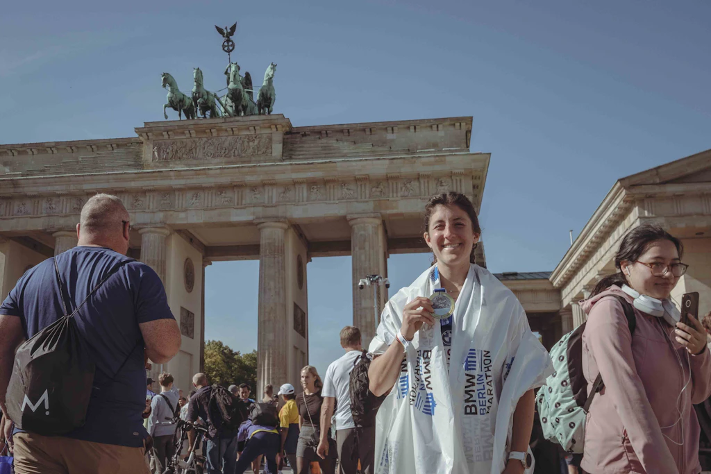 Eingehüllt in die Finisher-Folie, die Medaille in der Hand: Emily aus Michigan nach ihrem ersten Berlin-Marathon vor dem Brandenburger Tor.