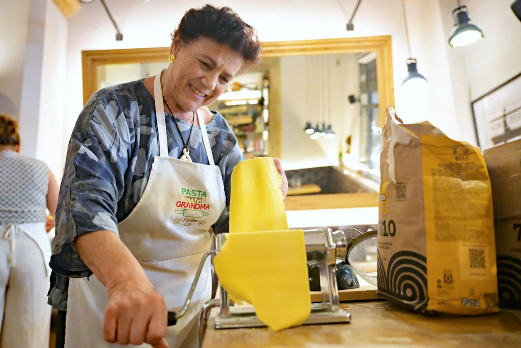 Rosella Mercuri (Nonna Rosi) dreht Nudelteig durch eine Nudelmaschine bei einem Pasta-Kochkurs. In den Sozialen Netzwerken trendet derzeit der Begriff Nonnamaxxing.