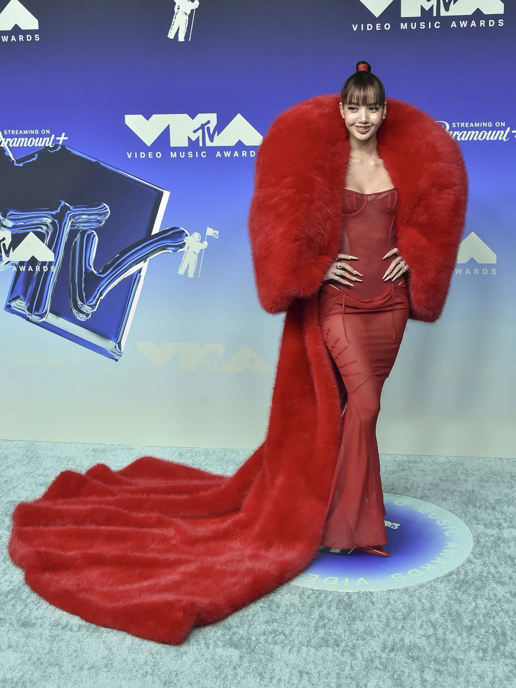 <strong>Flop:</strong> Die K-Pop-Sängerin Lisa setzte bei den VMAs auf Monochromie – verfehlte dabei jedoch die Balance. Ihr feuerroter Look wirkte überladen, da hier zwei extreme Welten unvorteilhaft aufeinanderprallten: Ein hautenges, transparentes Chiffon-Korsettkleid von The Attico traf auf einen wuchtigen, extrem breitschultrigen Kunstpelzmantel des Designers Quine Li. Während das Kleid durch Cut-outs und feine Transparenz eine filigrane Silhouette anstrebte, wurde diese von den massiven Proportionen und der endlosen Schleppe des Mantels förmlich erdrückt und erweckte Assoziationen an realitätsfernen Königen aus dem 18. Jahrhundert.