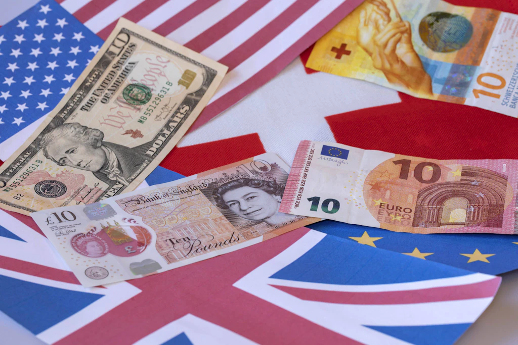 US-Dollar, britische Pfund, Schweizer Franken und Euro liegen auf den Flaggen der USA, Großbritanniens, der Schweiz und der EU. Für Banken aus Drittstaaten gelten ab Januar 2027 neue Regeln für deutsche Kunden. (Symboldbild)