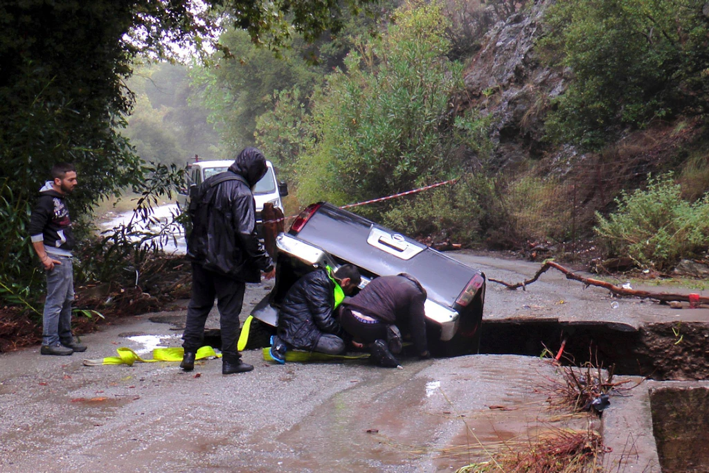 Anwohner versuchen auf Kreta, ein Auto aus einer vom Unwetter schwer beschädigten Straße zu bergen. Die Fahrbahn war durch die Wassermassen teilweise weggebrochen.