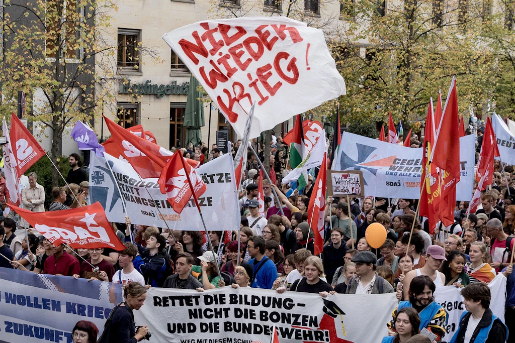 „Nie wieder Krieg“: Mit Fahnen und Transparenten demonstrieren Tausende am Tag der deutschen Einheit vor dem Brandenburg für Frieden und gegen Sozialabbau.