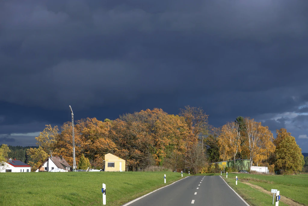 Leuchtendes Herbstlaub vor dunkler Wolkenwand: Ab Mittwochabend zieht eine Kaltfront über Deutschland, bis Freitag fallen die Höchstwerte auf 12 bis 18 Grad. (Symbolbild)