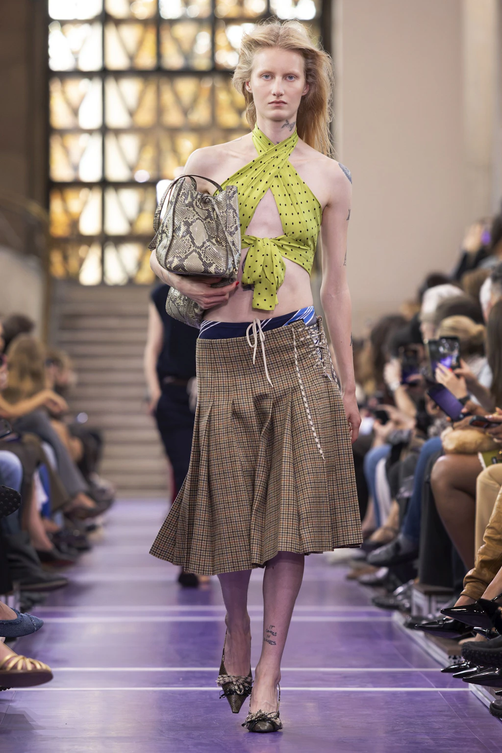 Keiner versteht es, so spielend leicht traditionelle Looks durch feine Details und hemmungsloses Layering so gekonnt aufzubrechen wie Miuccia Prada. Bei Pradas Schwesterlinie „Miu Miu“, die sich an ein jüngeres Publikum richtet, zeigt die Designerin Sportswear, gemixt mit Business-Silhouetten mit 70er-Jahre Flair. Herzstück der Kollektion: verzierte BH-Tops, die über Longsleeves und Pullovern straßentauglich werden. Statt Gürteln dominieren Kordeln und Seile, die Hosen und Röcke auf den Hüften halten. Dieses Schnürdetail zieht sich bis zu den begehrten New Balance x Miu Miu Sneakern durch.
