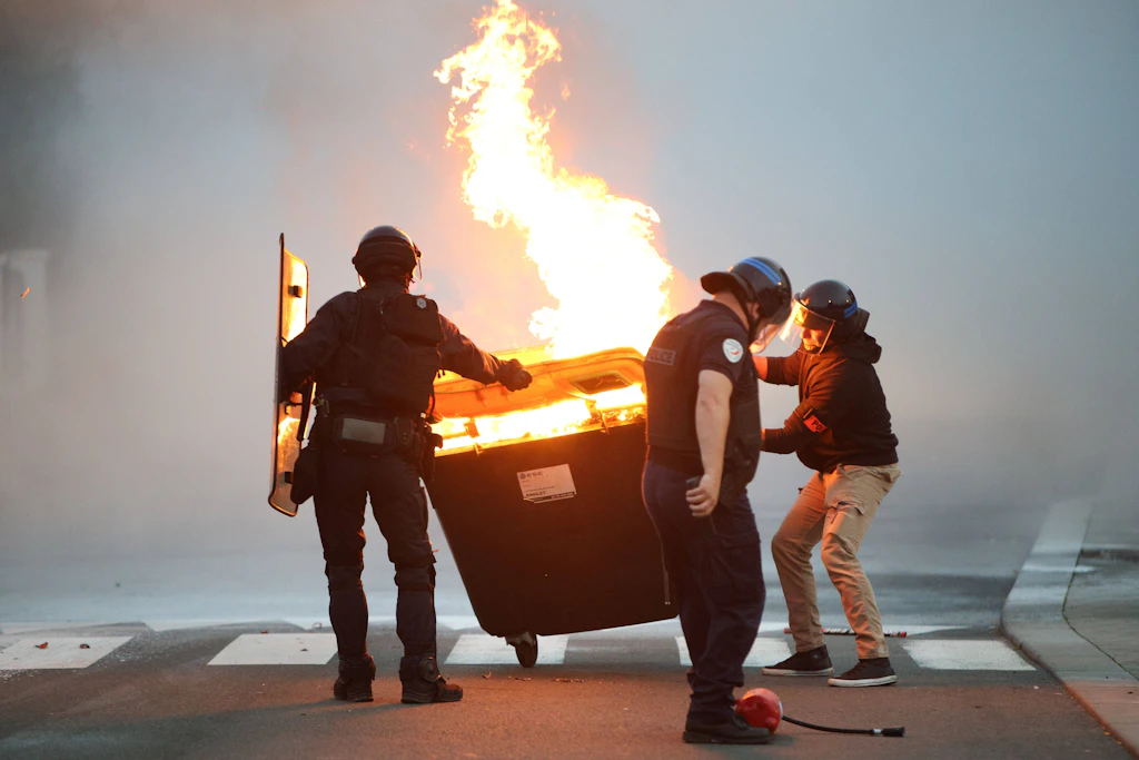 Polizisten schieben während eines Schülerprotests im südwestfranzösischen Anglet einen brennenden Müllcontainer beiseite.