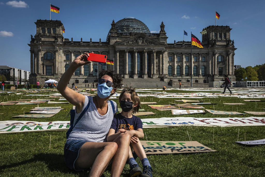 Mutter und Sohn machen ein Selfie vor dem Reichstag, dahinter Protesttransparente.