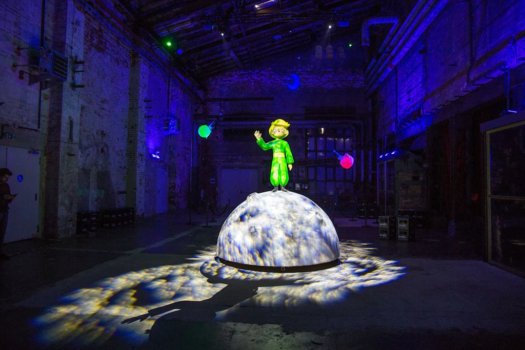 „Der kleine Prinz auf Reisen“ im Kunstkraftwerk Leipzig: Die Figur steht in der Schau auf einem leuchtenden Planeten.
