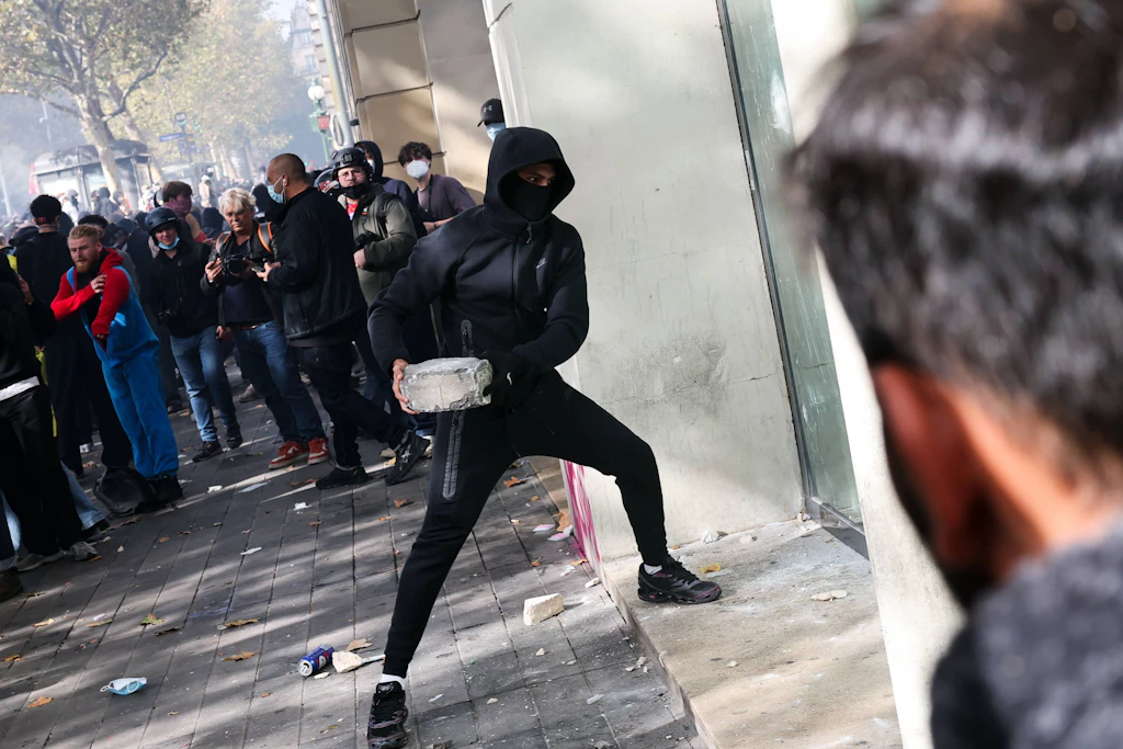 Ein Vermummter holt in Paris zum Wurf auf ein Schaufenster aus.