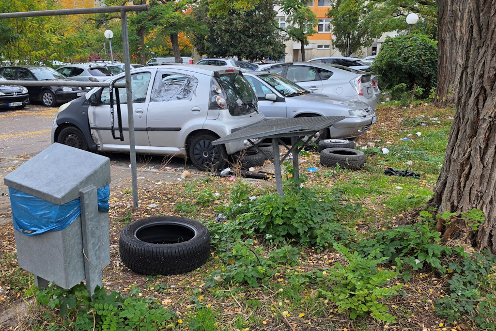 Zwischen Hochhaus und Hinterlassenschaften: Altreifen im Gras, Müll unter den Bäumen, ein Auto mit Klebeband statt Seitenscheibe. Vor dem Wohnblock türmt sich, was keiner wegräumt.