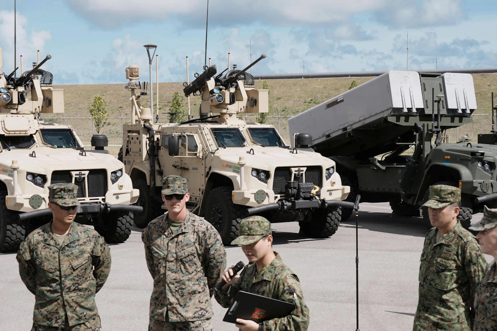 Amerikanische und japanische Militärangehörige vor Luftabwehrfahrzeugen und einem NMESIS-Raketenwerfer.