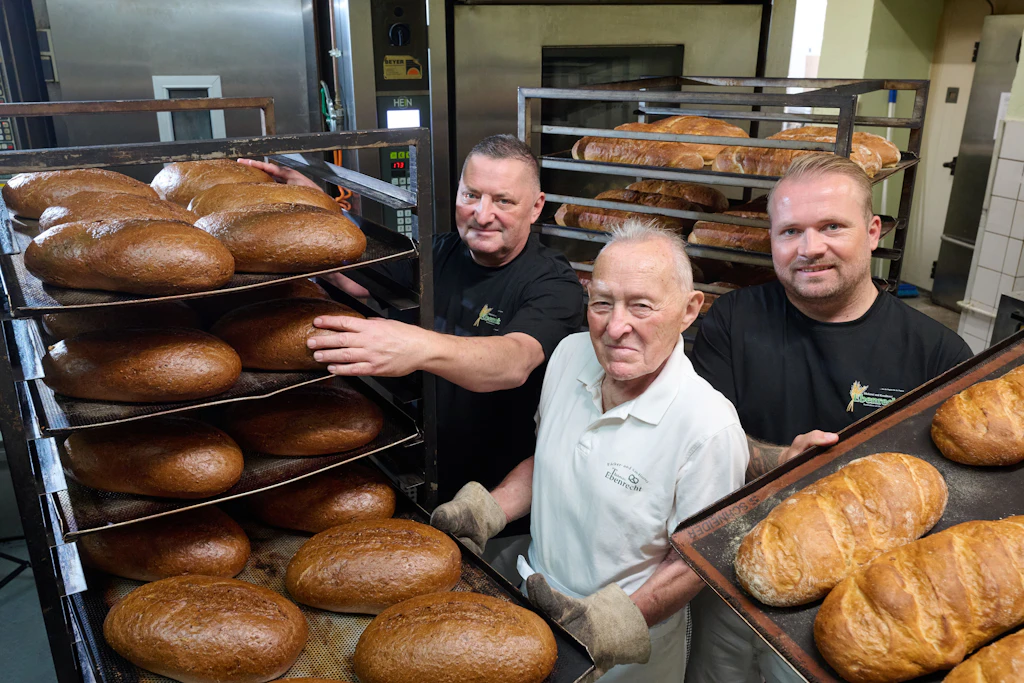Der 85-jährige Bäckermeister Gert Ebenrecht steht in der Backstube der Bäckerei und Konditorei in Teicha zwischen seinem Sohn Thomas (l.) und seinem Enkel Max. Allesamt haben das Bäckerhandwerk von der Pike auf gelernt.