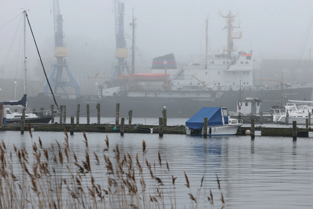 Boote und der Museums-Eisbrecher „Stephan Jantzen“ im Stadthafen an der Warnow verschwinden im Nebel.