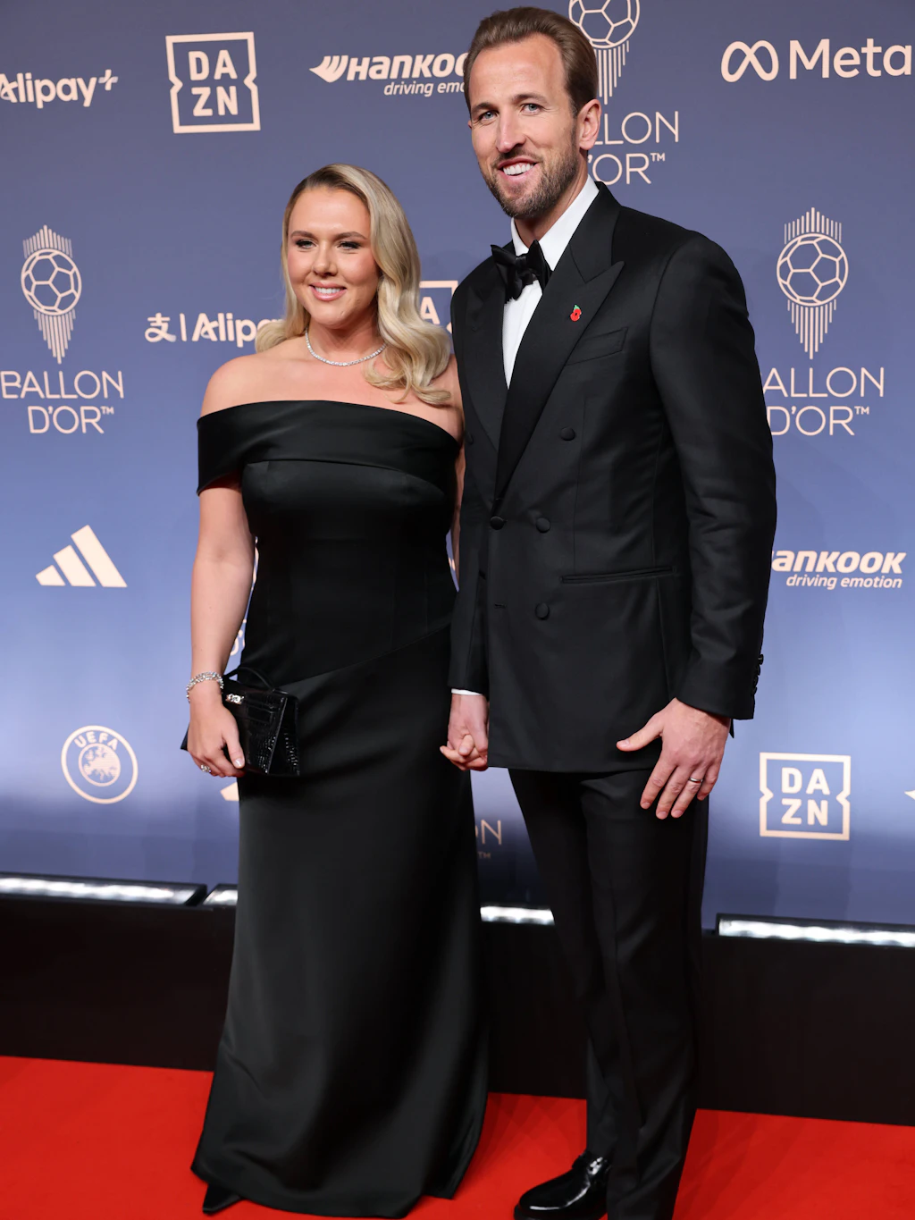 <strong>Top:</strong> Der Star des Abends, Harry Kane, erscheint in zeitloser, schlichter Eleganz auf dem roten Teppich. Der FC-Bayern-Spieler trägt einen zweireihigen Smoking von Thom Sweeney mit schwarzer Fliege und einer Mohnblumen-Anstecknadel zum Gedenken an die gefallenen Soldaten des Commonwealth. Der Look ist zurückhaltend, überzeugt aber durch kleine Details wie die mit Satin überzogenen Knöpfe. Seine Frau Katie führt den Black-Tie-Look mit einem schulterfreien schwarzen Satinkleid fort. Ein wahrer Gewinnerlook.