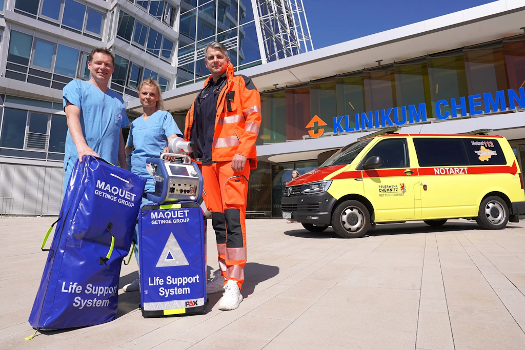 ECMO-Team startet: Drei Mitglieder des Klinikums Chemnitz präsentieren vor dem Eingang die mobile Ausrüstung für den Einsatz bei Schwerkranken.