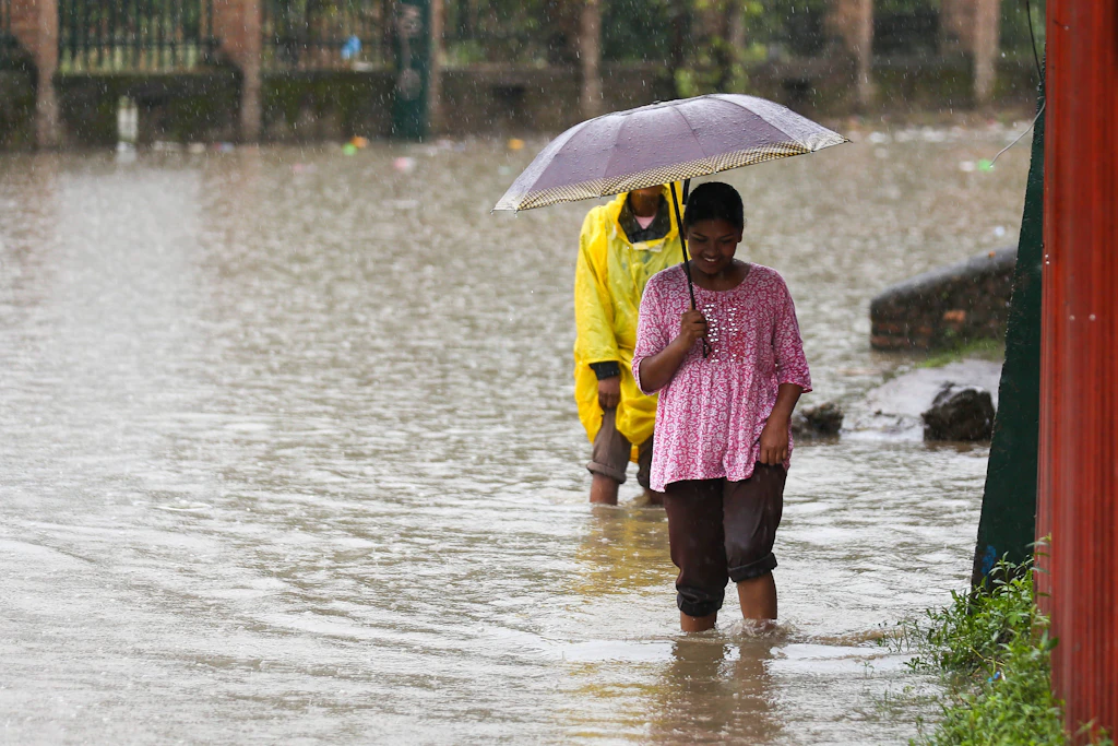 Menschen waten durch die überfluteten Straßen von Kathmandu in Nepal. Nach heftigen Regenfällen war der Bagmati-Fluss über die Ufer getreten. Oxfam warnt vor den besonders schweren Folgen solcher Katastrophen für ärmere Bevölkerungsgruppen.