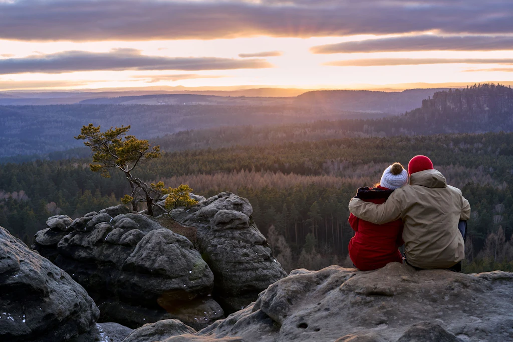 Wintertour in der Sächsischen Schweiz: Auf dem Gohrisch genießen zwei Menschen den Blick ins Tal bei Sonnenuntergang.