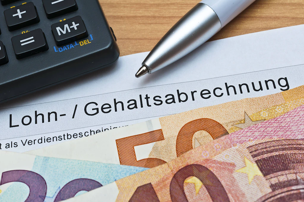 Eine Lohn- und Gehaltsabrechnung mit Geldscheinen: Wer mehr als 5812,50 Euro brutto verdient, zahlt 2027 höhere Beiträge für Krankenkasse und Rente.