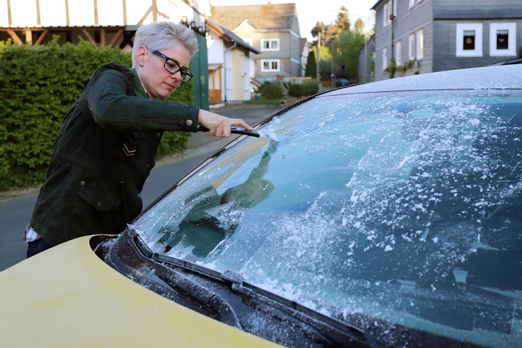 Eine Autofahrerin kratzt am Morgen die vereiste Frontscheibe ihres Wagens frei. Wer dabei den Motor laufen lässt, um schneller warm zu werden, riskiert 80 Euro Bußgeld. (Symbolbild)