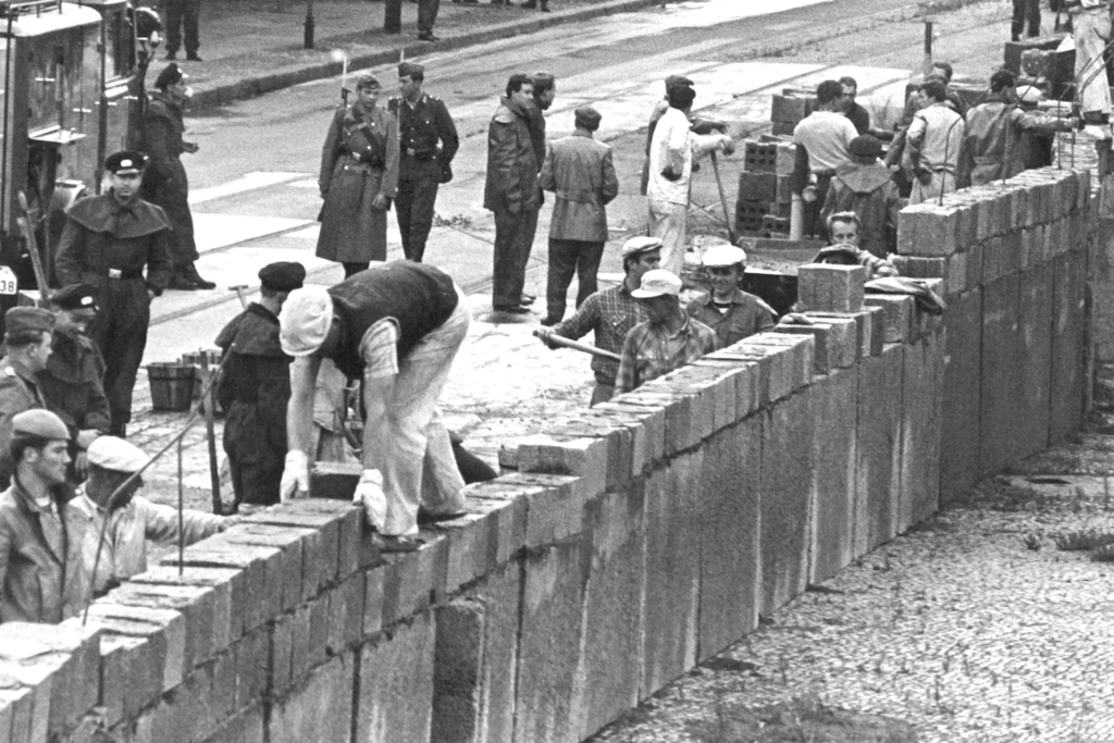 August 1961. Bauarbeiter errichten die Berliner Mauer. Sie werden von Soldaten und Grenzpolizisten bewacht.